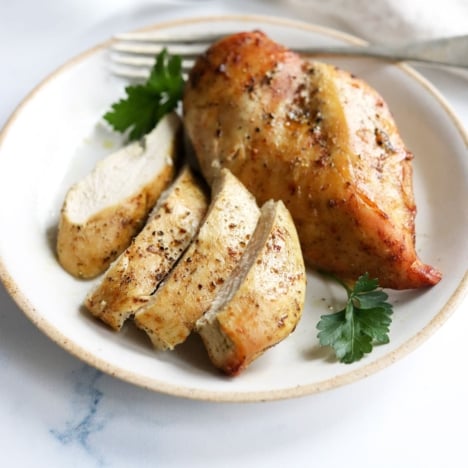 air fryer chicken breasts on white plate with 1 sliced