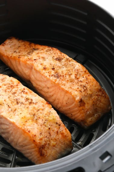 two salmon fillets cooked in a black air fryer basket.