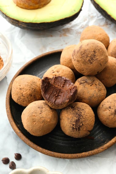 avocado truffles coated in cocoa powder on a black plate.