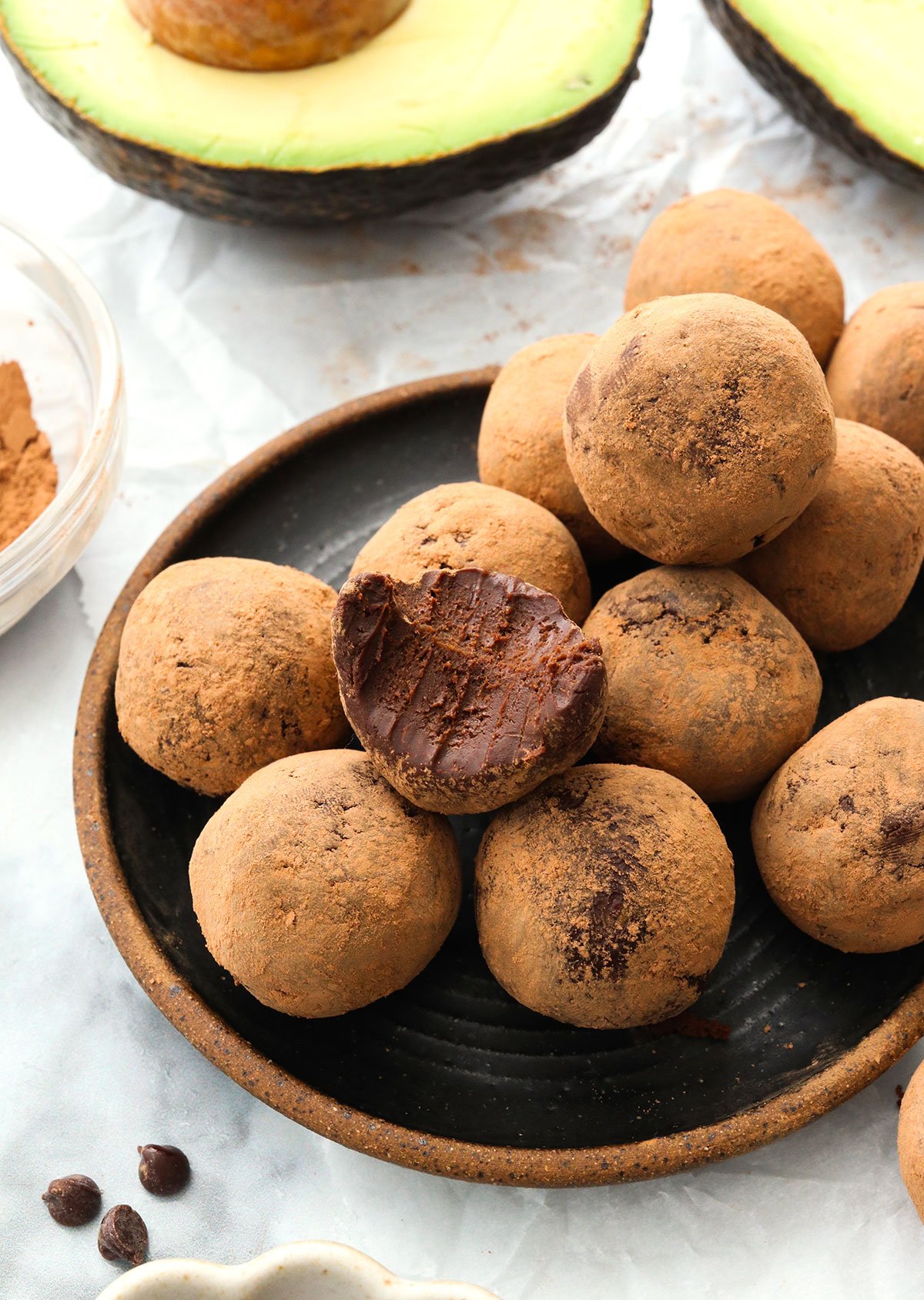 avocado truffles coated in cocoa powder on a black plate.