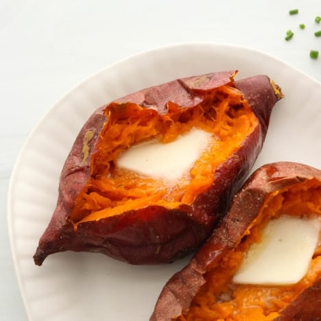 two baked sweet potatoes on a white plate topped with butter.