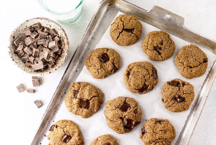 buckwheat chocolate chip cookies on a cookie sheet with a bowl of chocolate chunks next to it