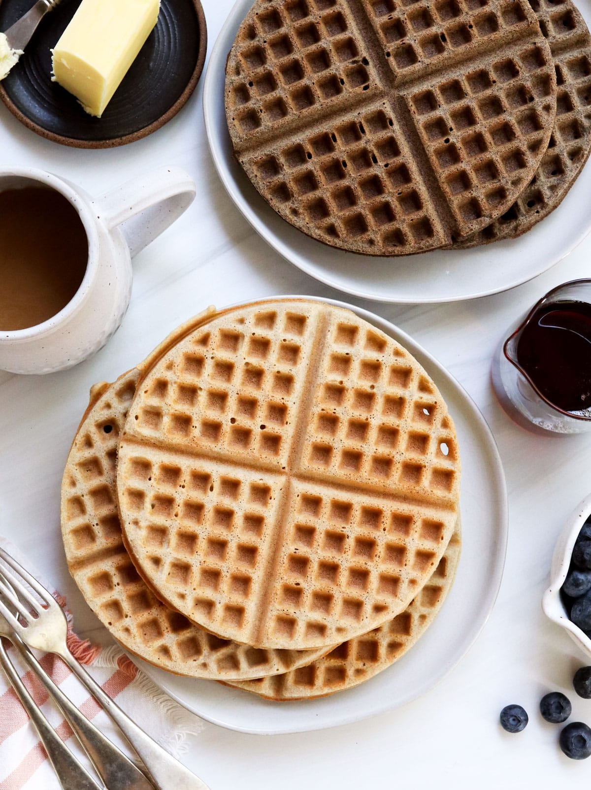 stack of light and dark buckwheat waffles served with fruit and syrup.