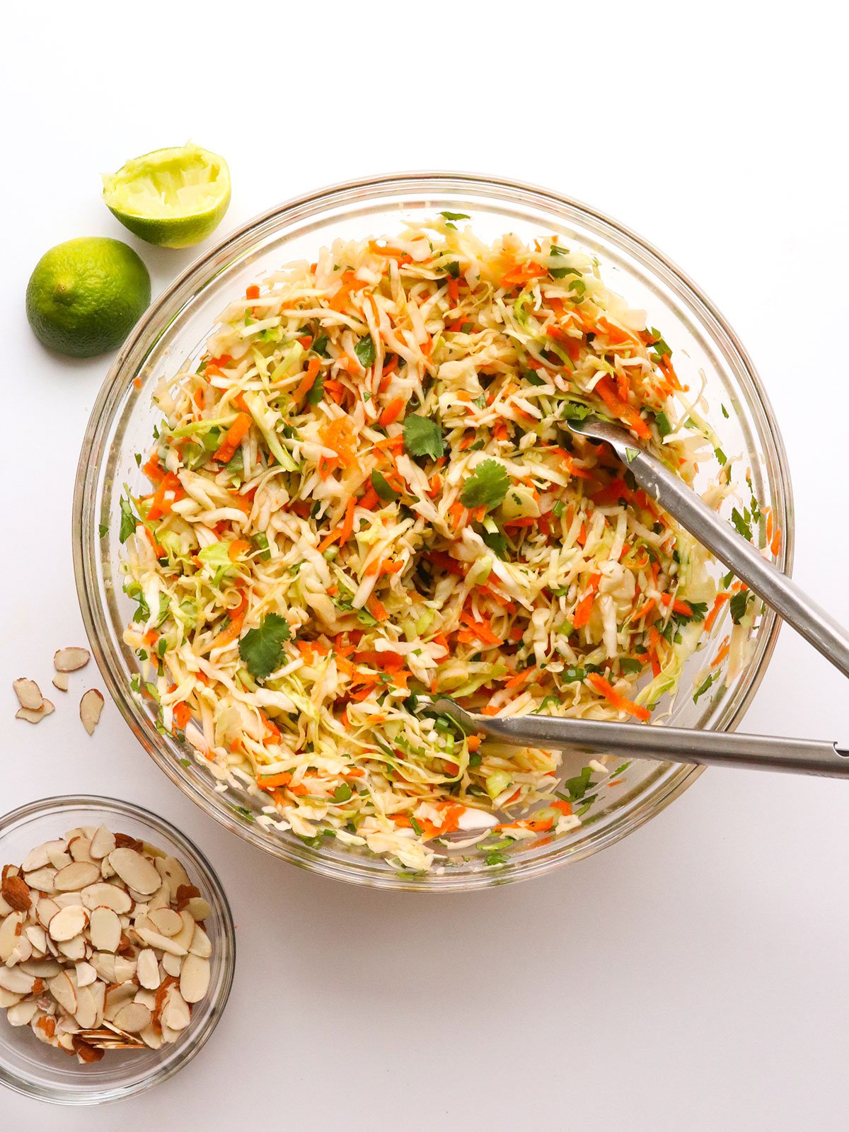 cabbage salad mixed with metal tongs in a glass bowl.