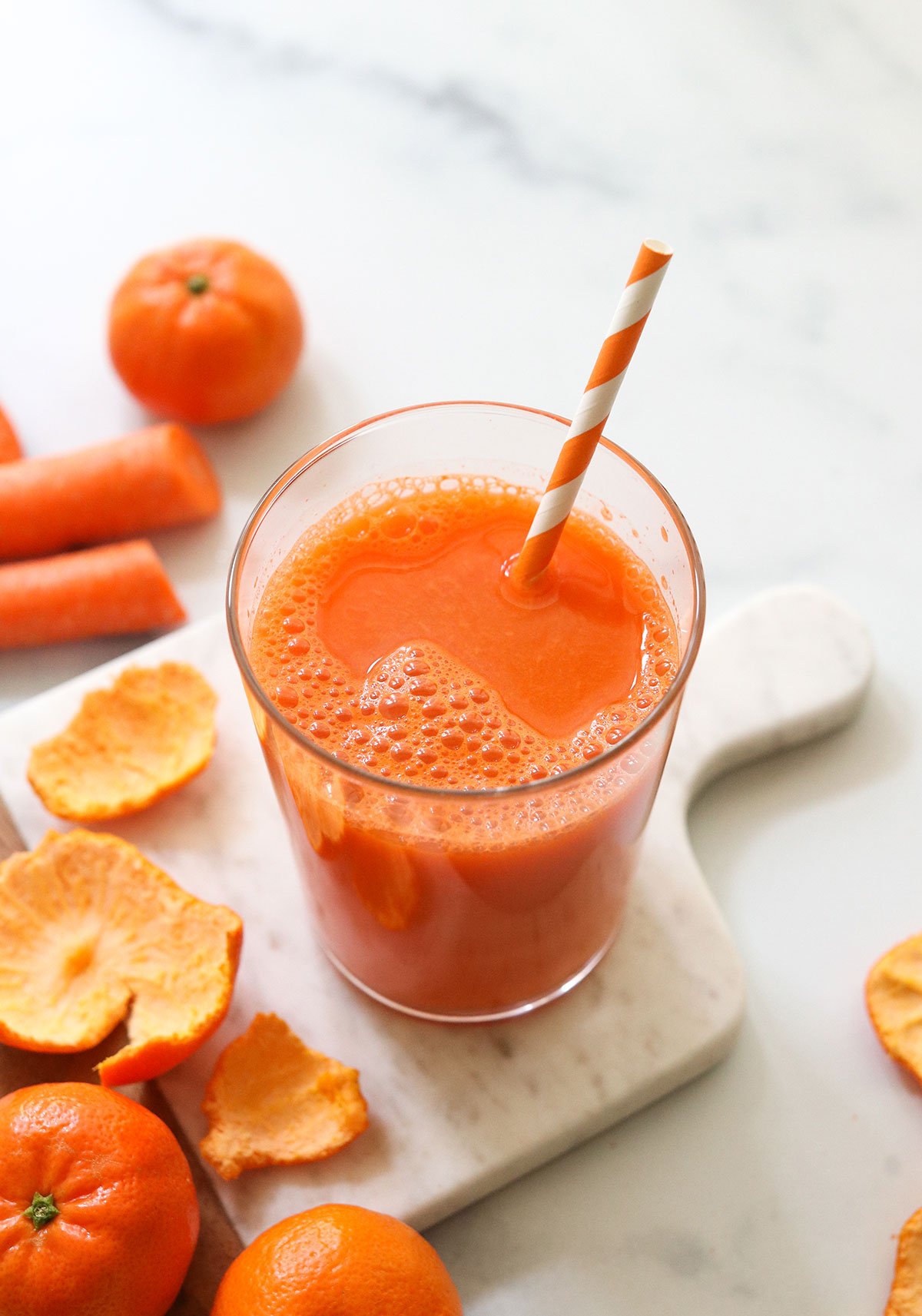 Carrot juice served with a striped straw on a white marble board.