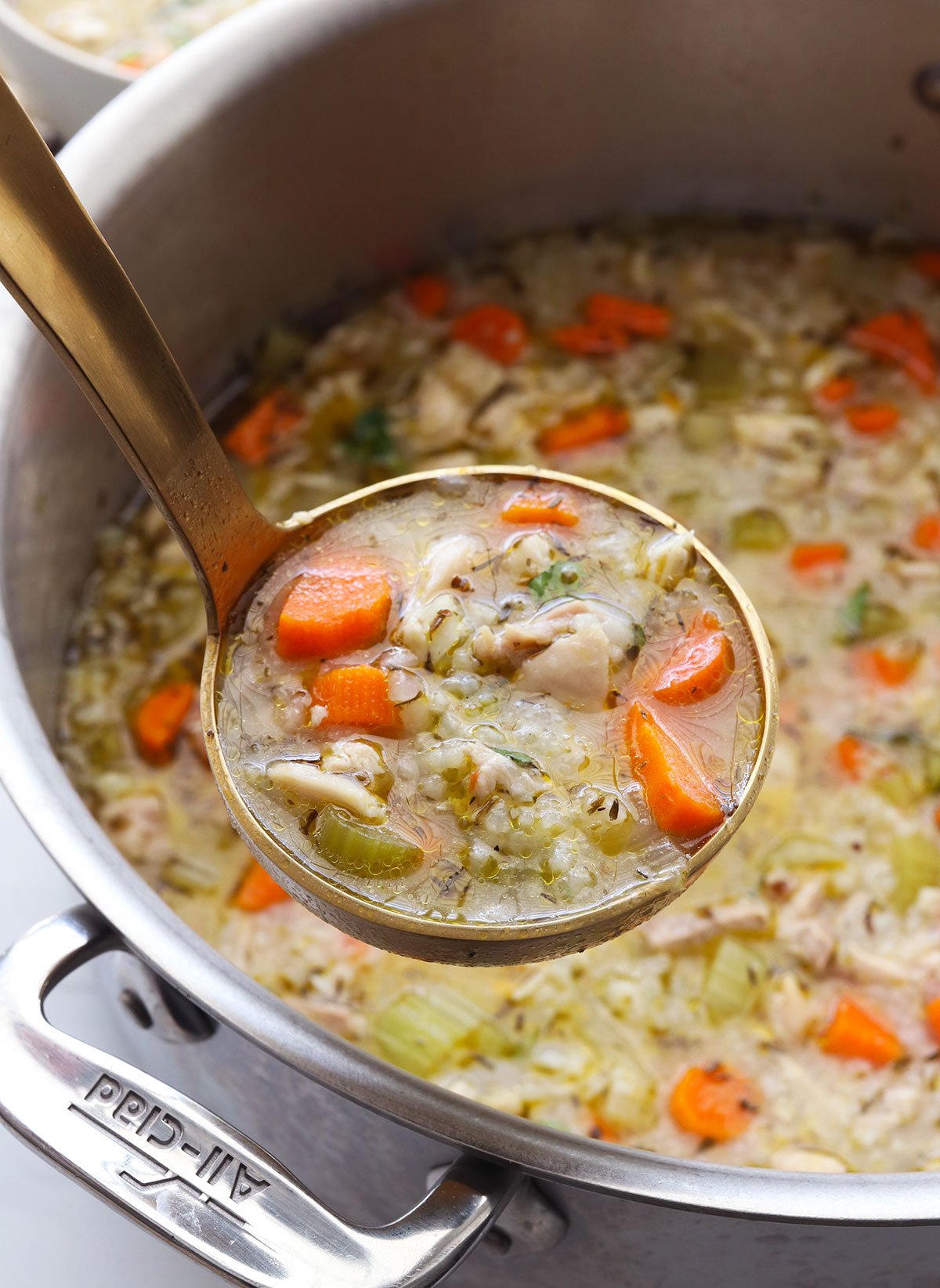 chicken and rice soup lifted up on a gold ladle.