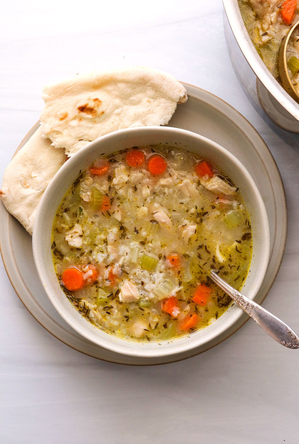 chicken and rice soup served in a white bowl with bread.