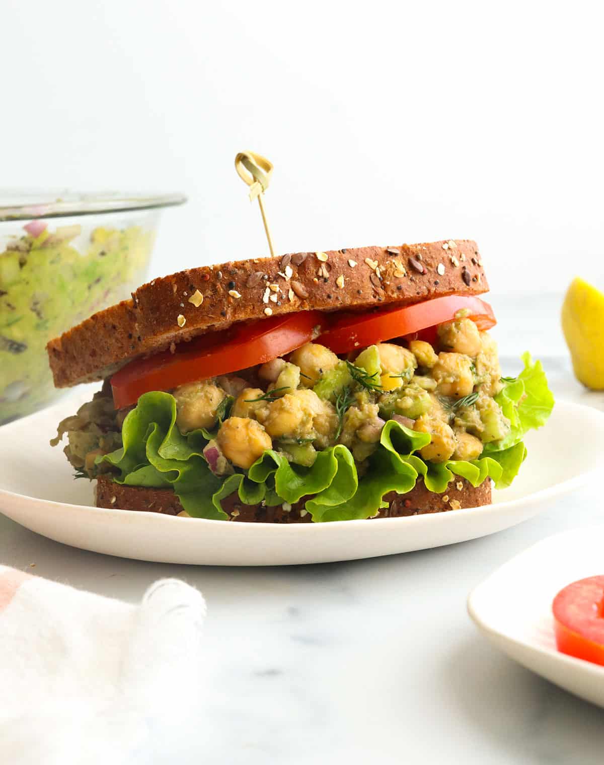 chickpea salad sandwich with sliced tomatoes and a toothpick in the bread.