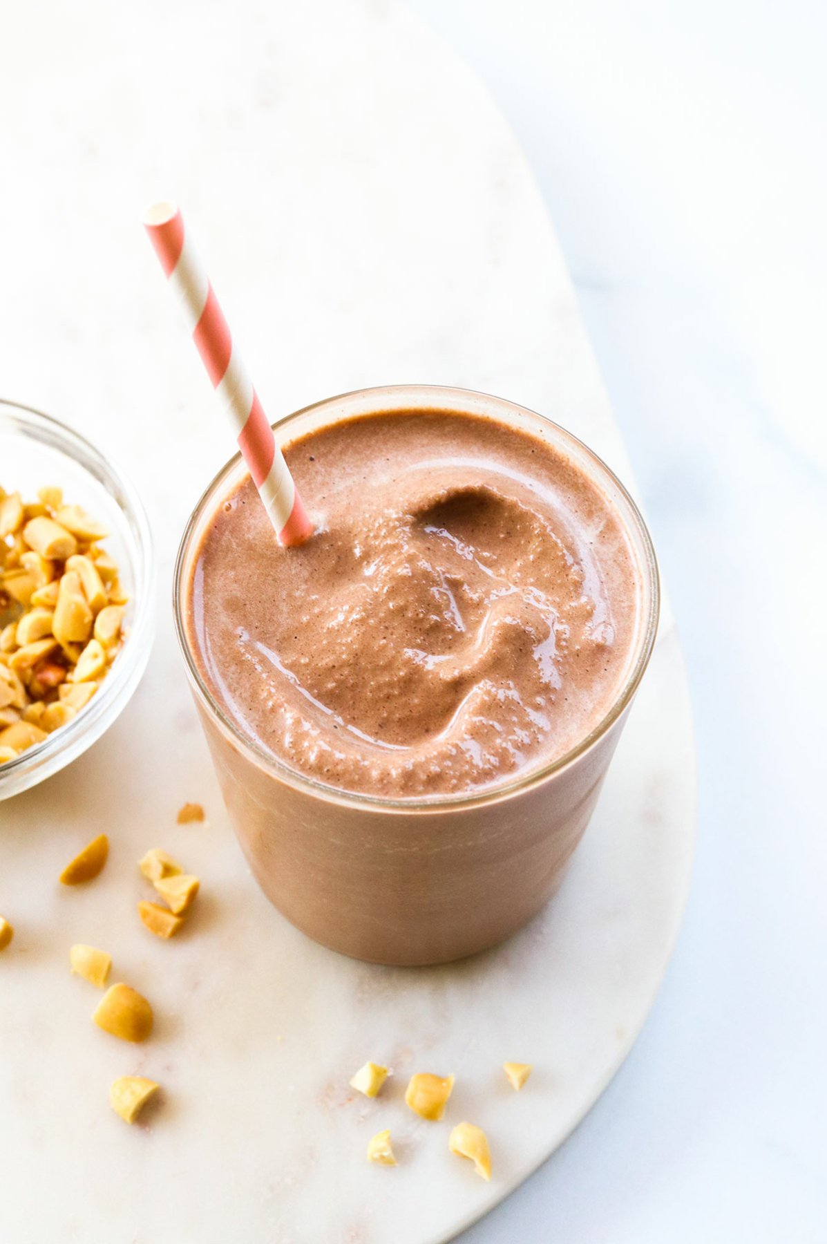 Chocolate peanut butter banana smoothie in a glass with a pink striped straw.