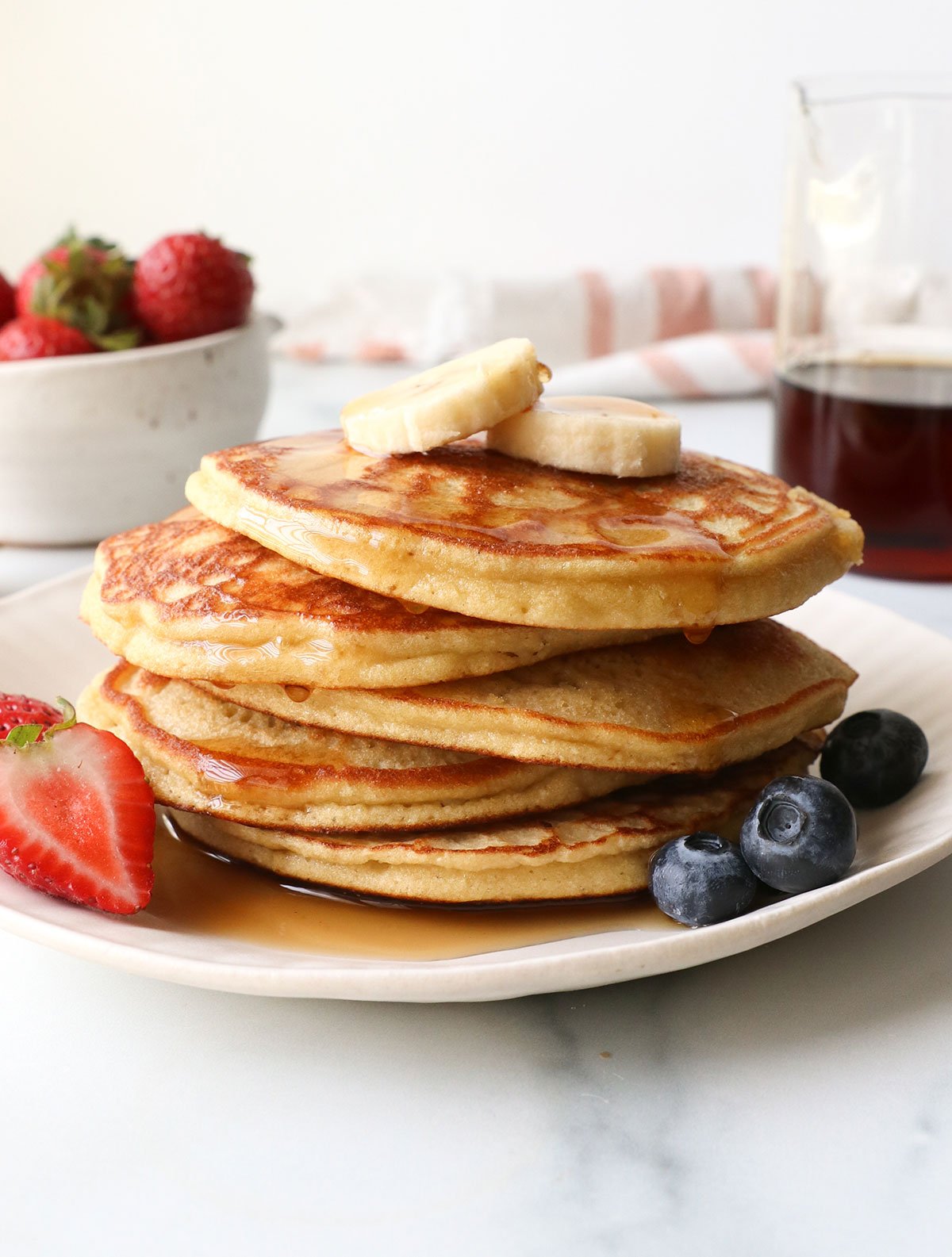 coconut flour pancakes stacked on a plate with fruit.