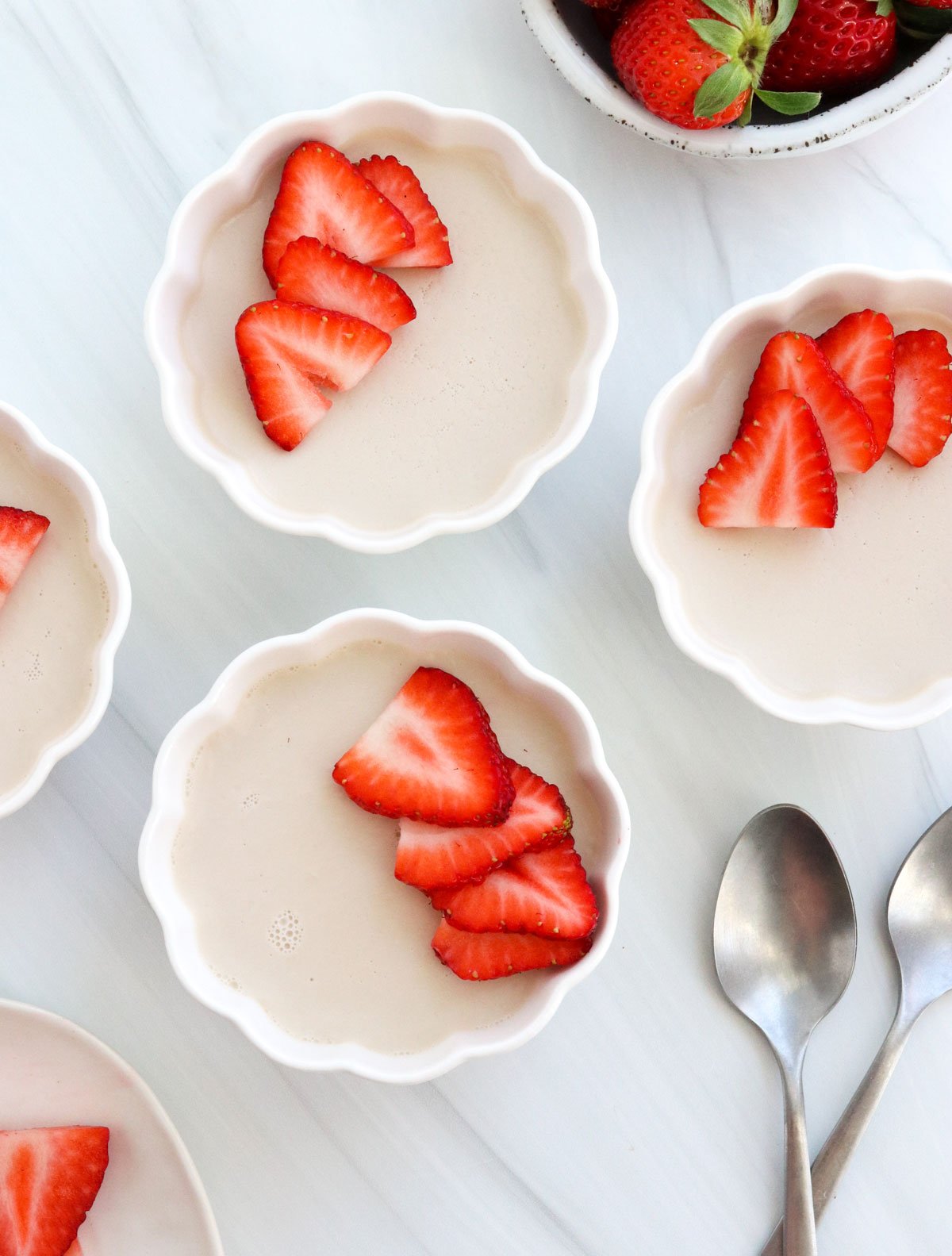 coconut panna cotta in bowls with strawberries on top.