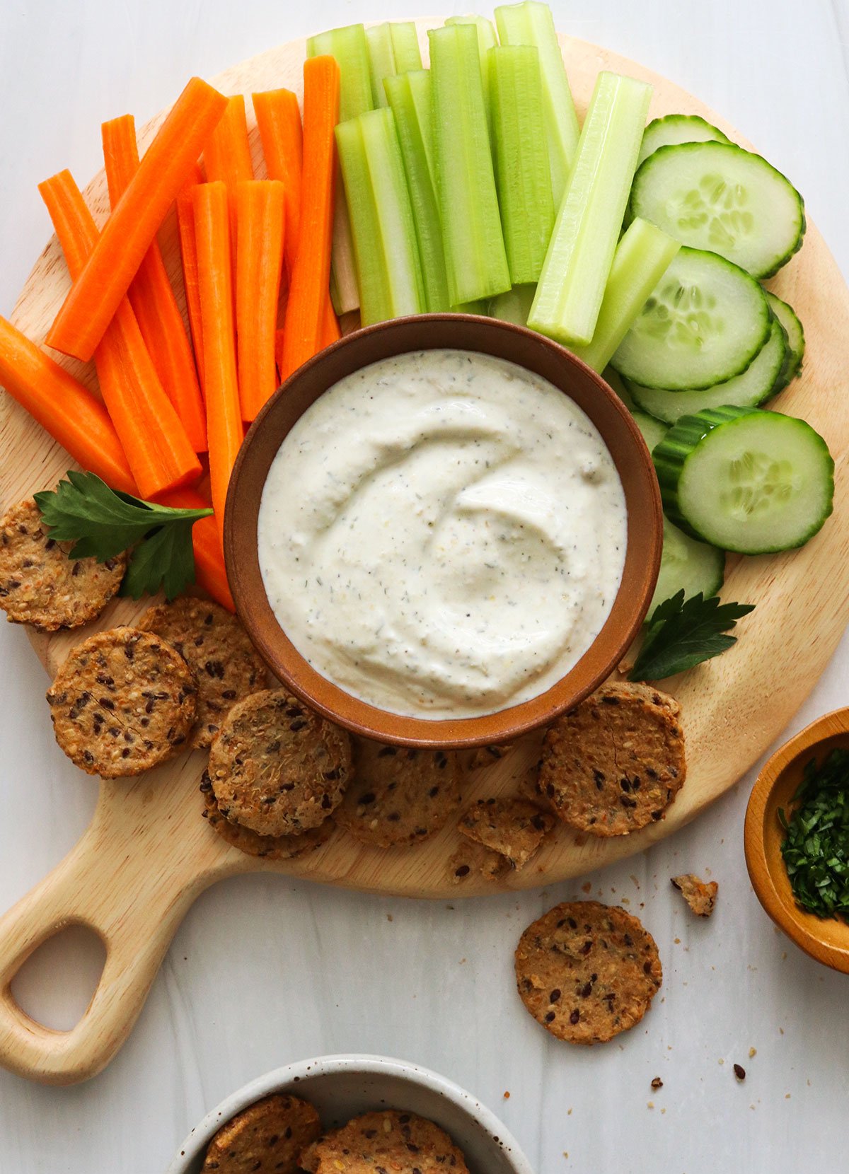 cottage cheese dip in a brown bowl surrounded by sliced veggies and crackers.