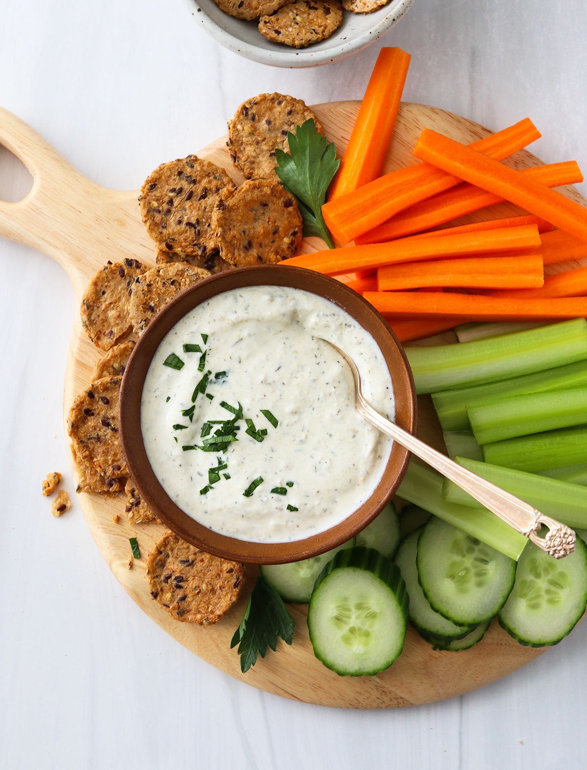 Cottage cheese dip served with sliced veggies and crackers on a platter.