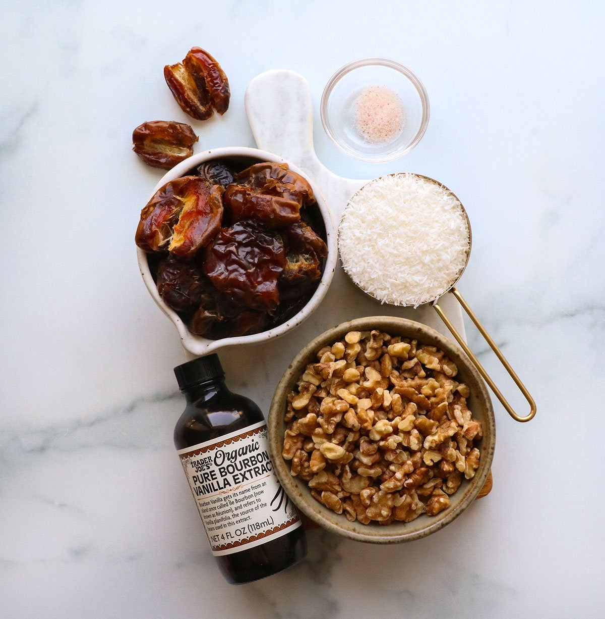 dates, walnuts, coconut, salt, and vanilla extract on a white board.