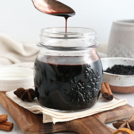 elderberry syrup pouring off of a spoon into jar