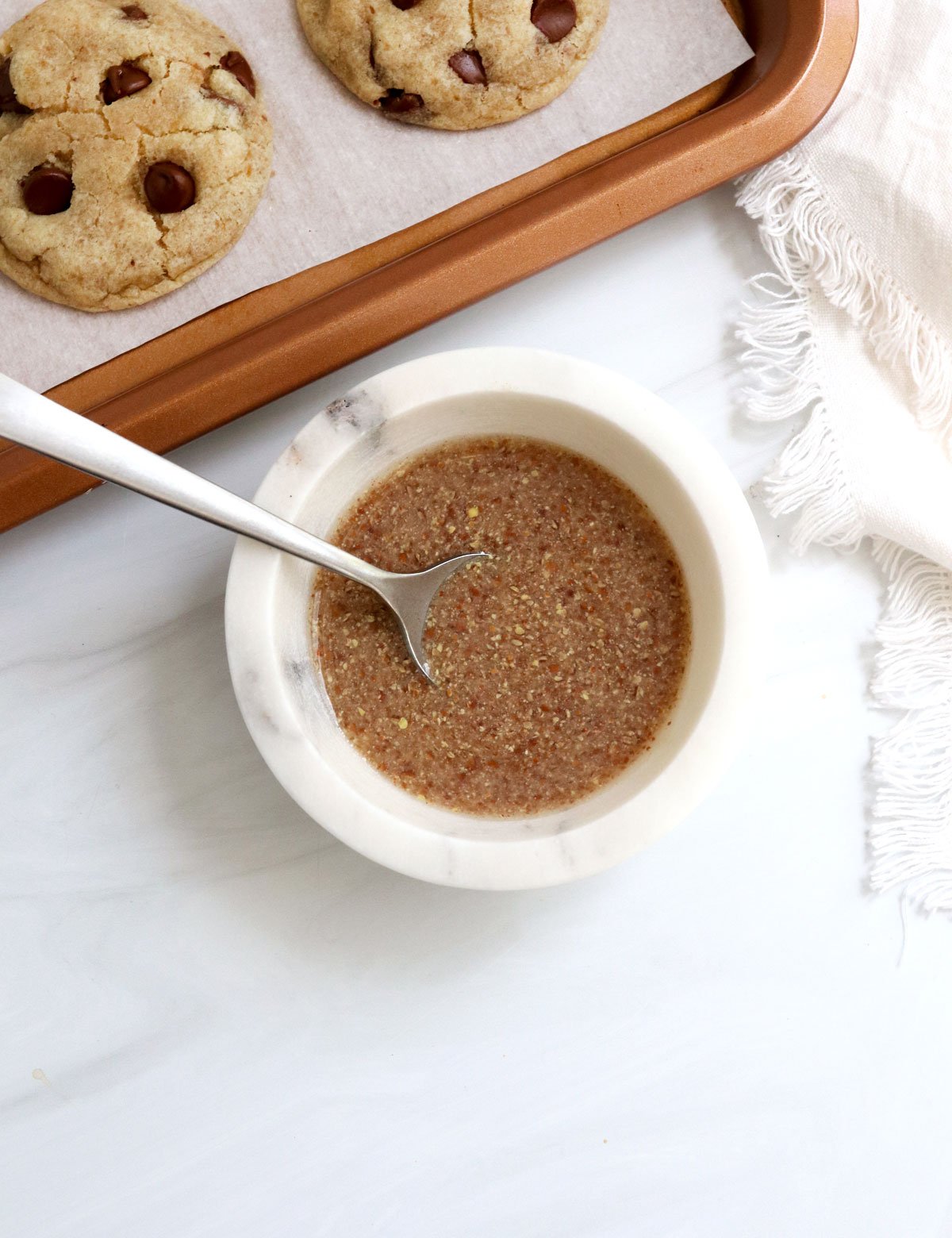 flax egg in a white bowl next to a pan of cookies.