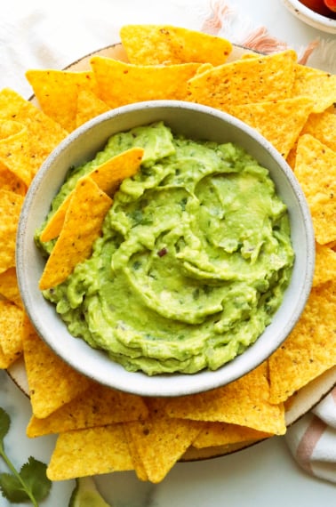 Closeup of the best guacamole served in a bowl with yellow corn chips.