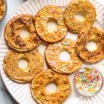 apple slices that look like donuts with sprinkles, granola, hemp hearts, and shaved chocolate on top.