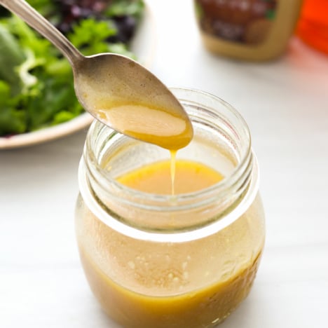 honey dijon vinaigrette dripping off a spoon into a jar.