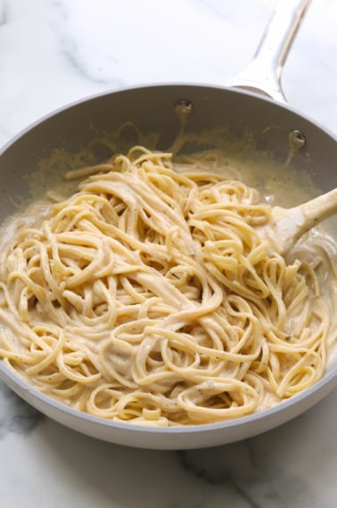 hummus pasta tossed with a white spatula in a gray skillet.