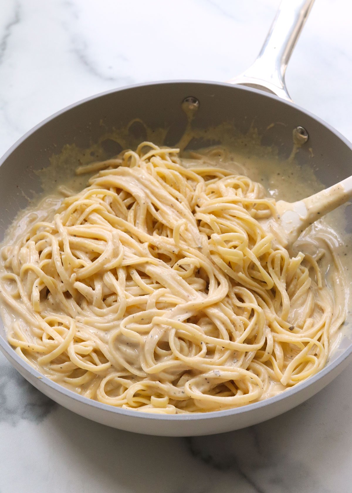 hummus pasta tossed with white spatula in a gray skillet.