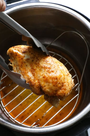 Juicy instant pot chicken breast lifted up with tongs.