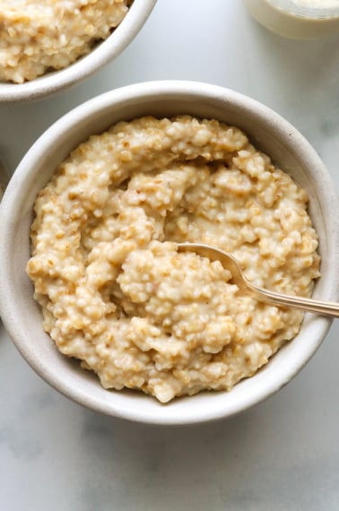 two white bowls filled with instant pot steel cut oats and a spoon.