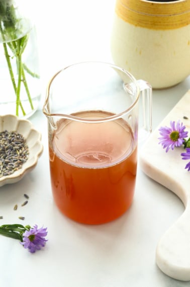 honey lavender syrup in a glass jar near purple flowers.