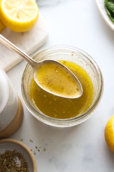 spoon lifted up with lemon vinaigrette over a jar.