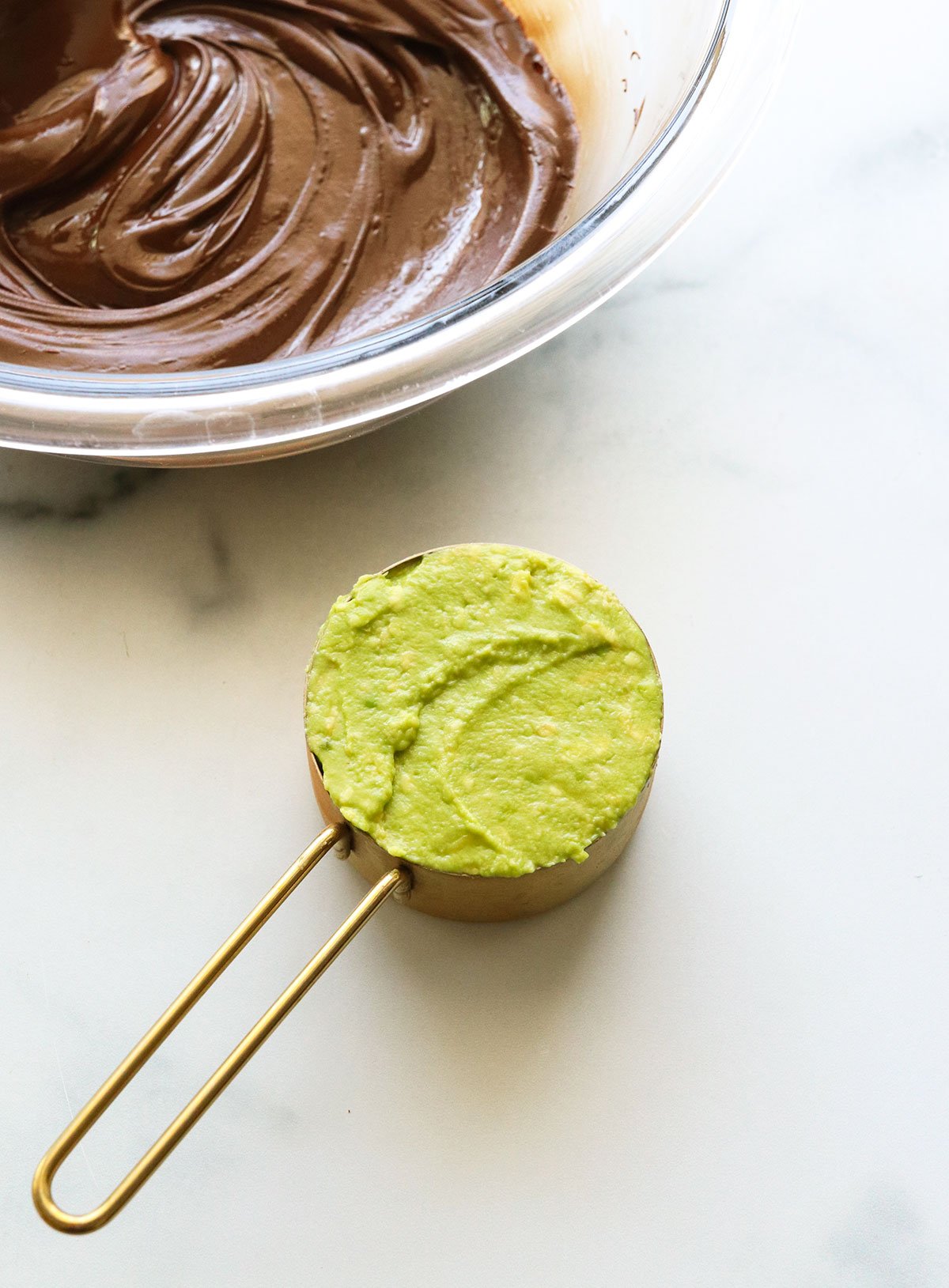 mashed avocado measured in a cup next to melted chocolate.