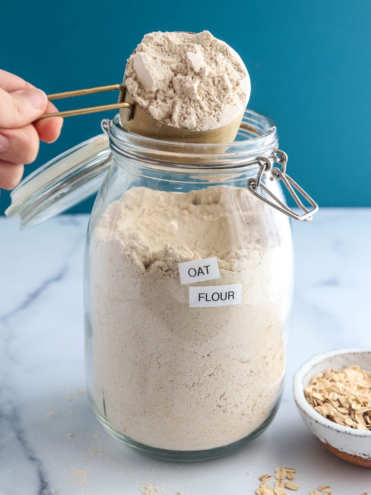 oat flour scooped from jar with blue background