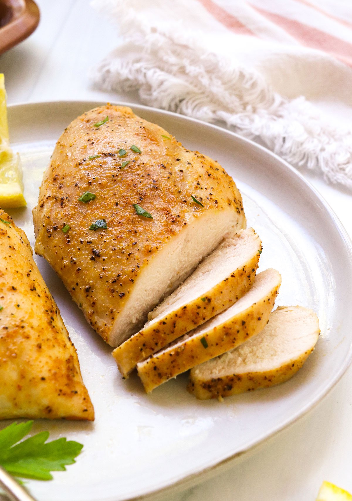 oven baked chicken breast sliced on a white plate with parsley.