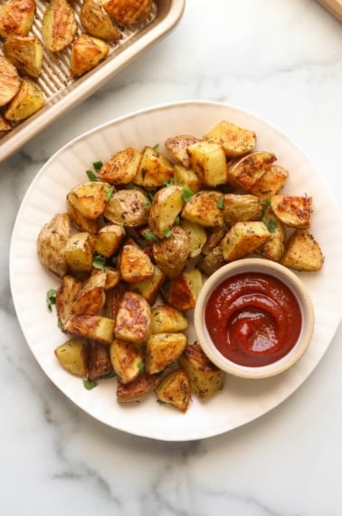 oven roasted potatoes on a white plate with a side of ketchup.