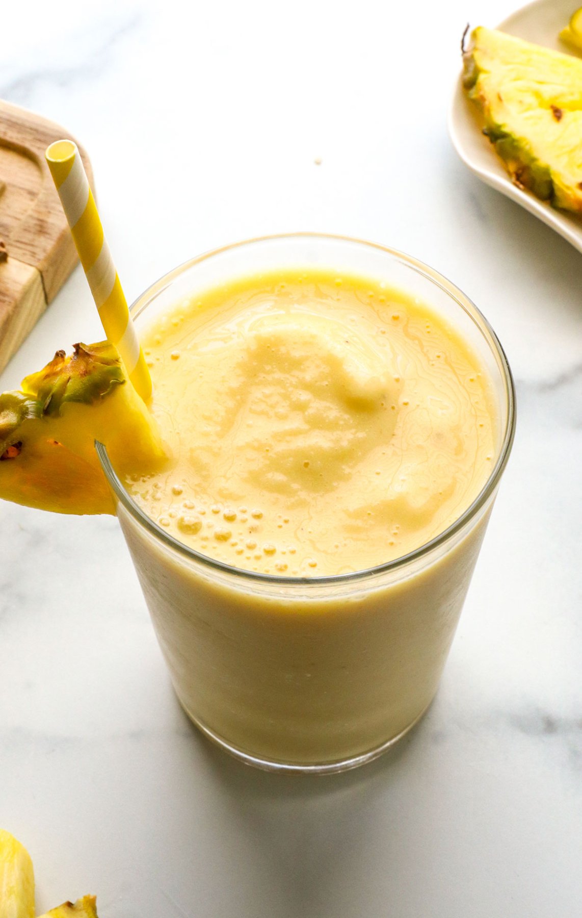 slushy pineapple smoothie in a glass with a yellow straw.