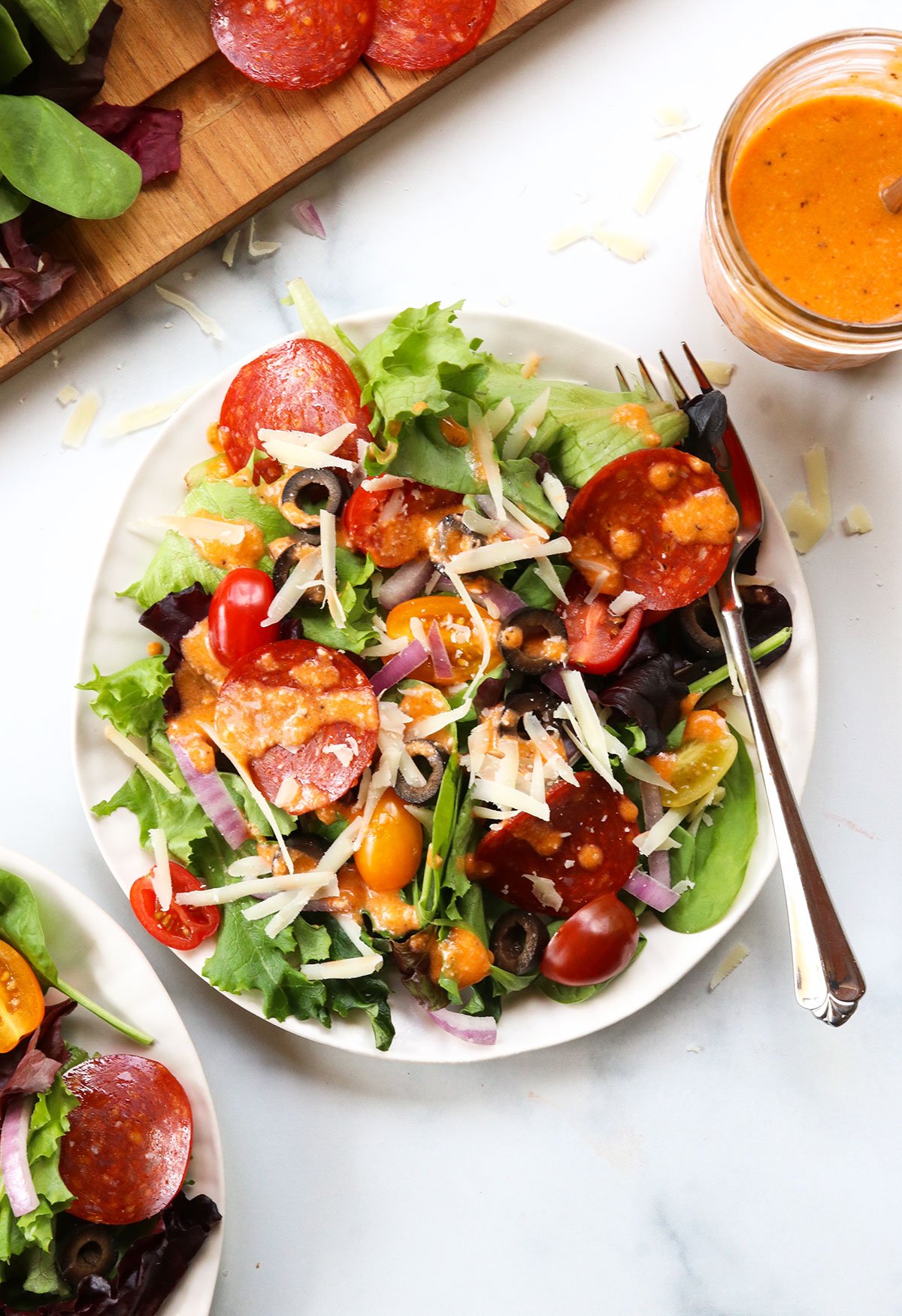 Pizza salad served on a white plate with a fork next to a jar of pizza salad dressing.