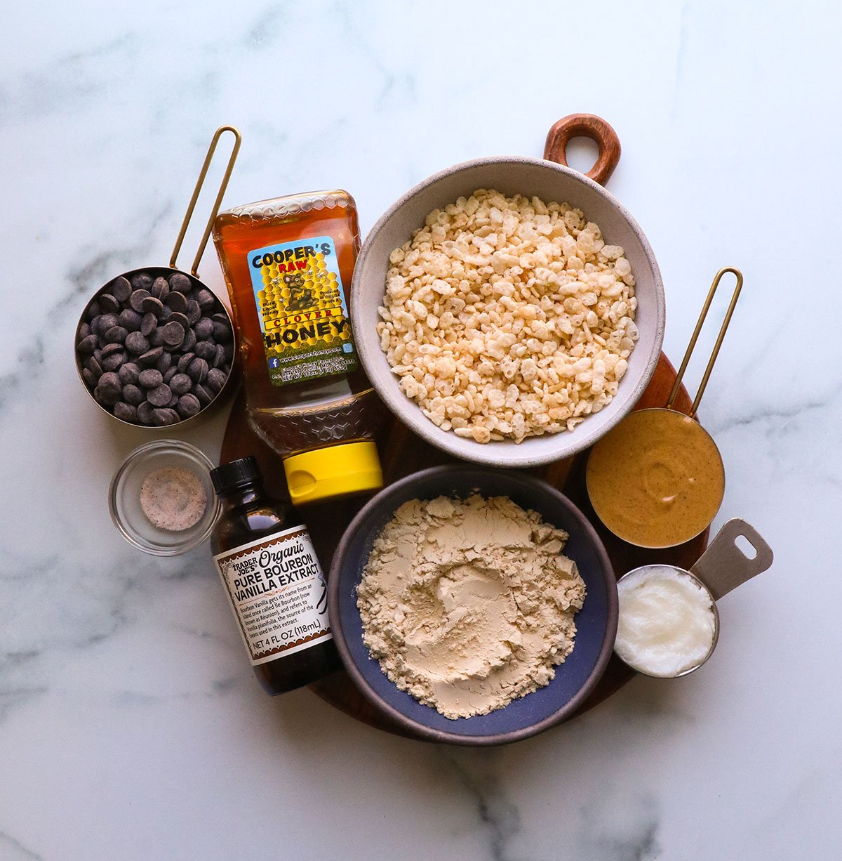 bowl of rice crispy cereal, protein powder, honey, peanut butter, coconut oil, and more on a white board.