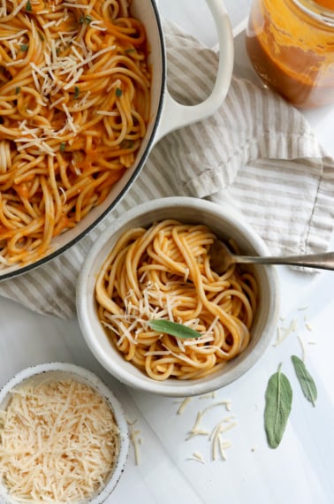 bowl of pumpkin pasta next to a white skillet