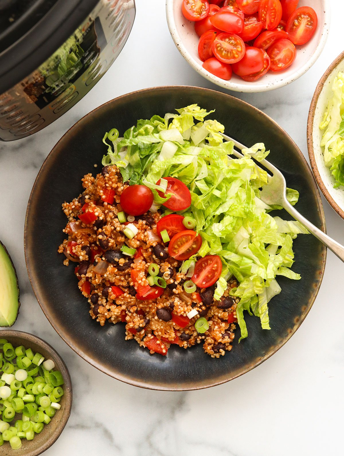 quinoa burrito bowls in a black bowl with shredded lettuce and tomatoes.