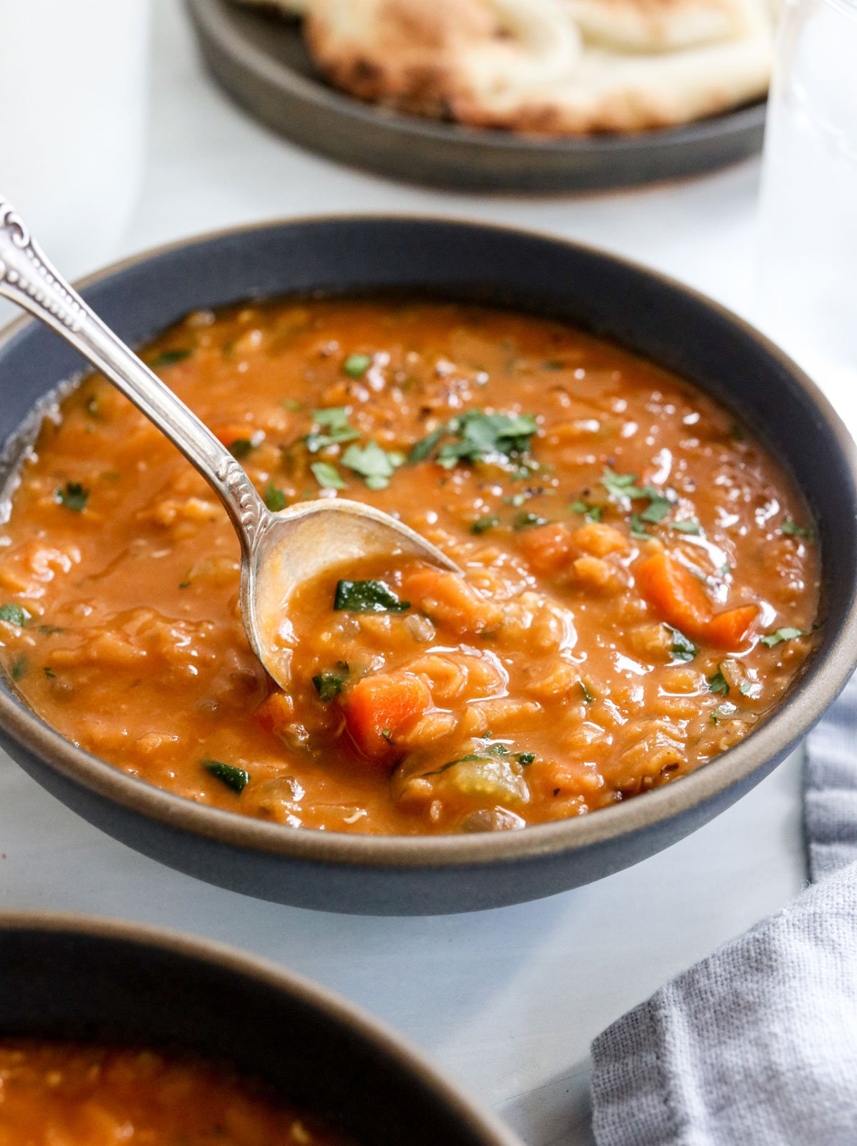 spoon lifting up the red lentil soup from a black bowl.