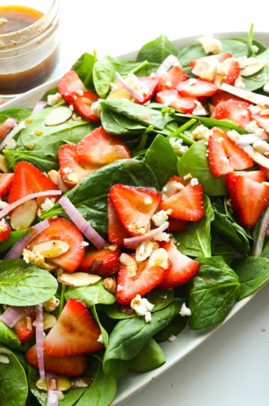 spinach strawberry salad tossed with balsamic dressing on an oval plate.