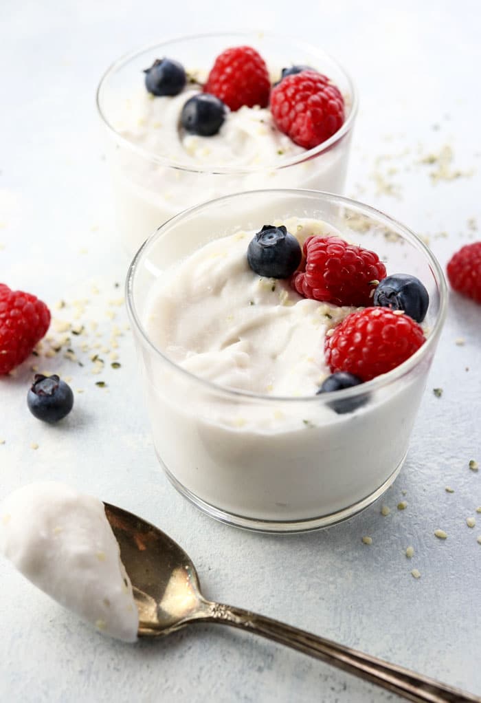 two cups of coconut milk yogurt topped with fruit and a spoon