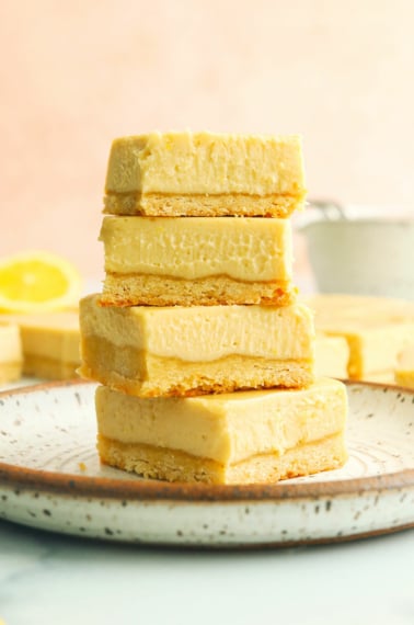 vegan lemon bars stacked on a white plate with pink background.