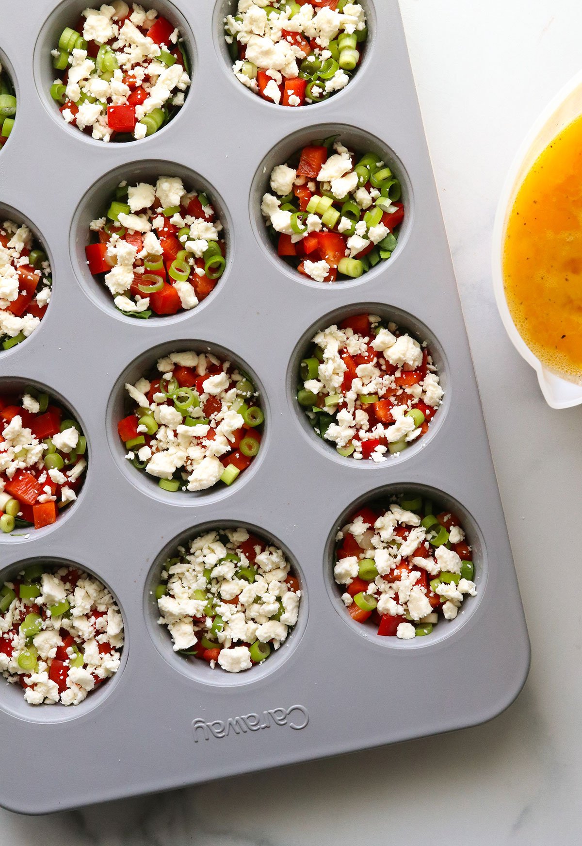 diced veggies and feta filling a muffin tin.