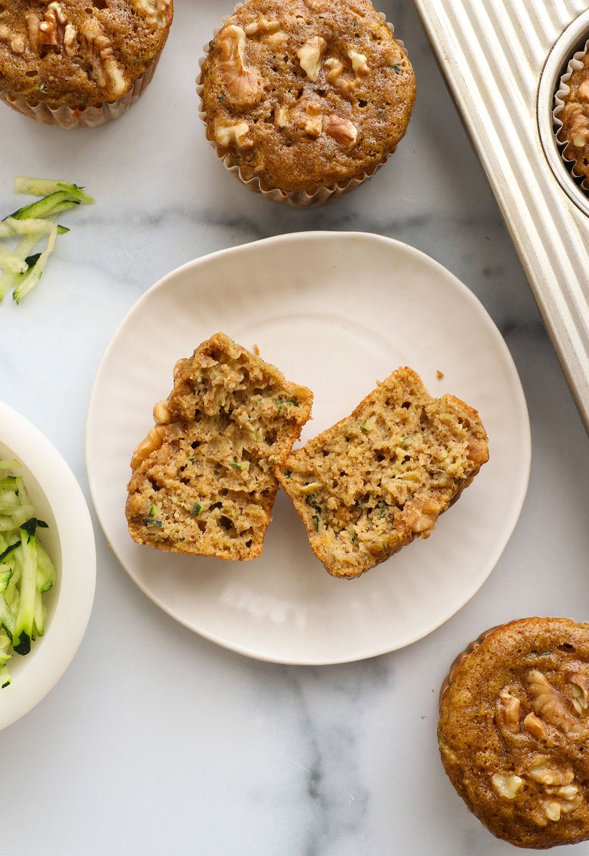 zucchini muffin split in half on a white plate.